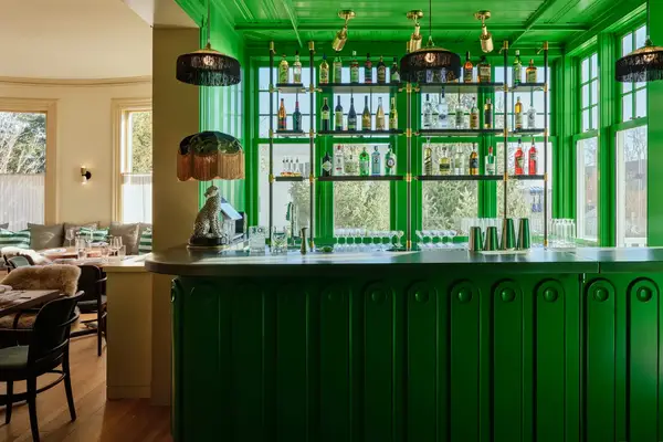 Interior of a bar with a green counter and backlit shelves stocked with bottles
