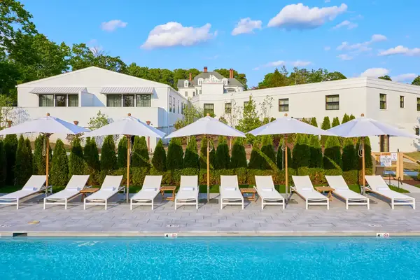 A row of poolside lounge chairs and umbrellas with white buildings in the background