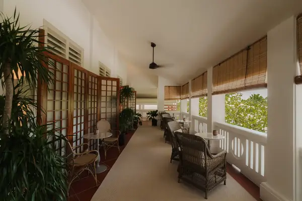 Outdoor dining area with wicker chairs and tables under a covered walkway, surrounded by tropical plants overlooking greenery