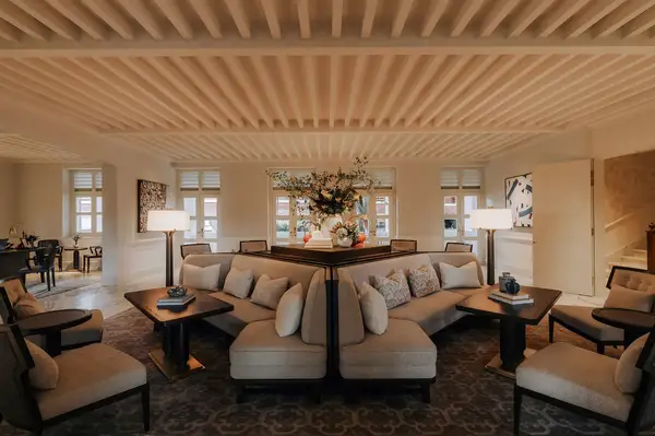 A spacious and well-lit lounge area with modern furniture and decor, featuring multiple seating arrangements in a symmetrical layout