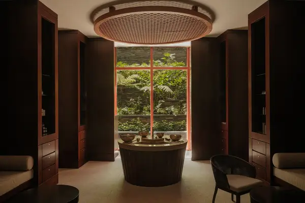 Spa treatment room interior with central table and large window showcasing a serene outdoor garden view