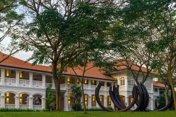 The exterior of a historic building surrounded by trees, with a contemporary sculpture in the foreground