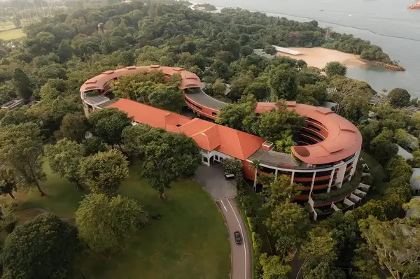 Aerial view of a winding hotel surrounded by greenery, beachfront nearby