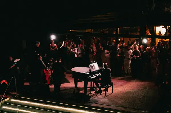 An evening outdoor performance with a pianist at a grand piano and an audience watching