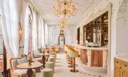 Elegant interior of a restaurant with a bar, ornate chandeliers, and seating areas by large windows