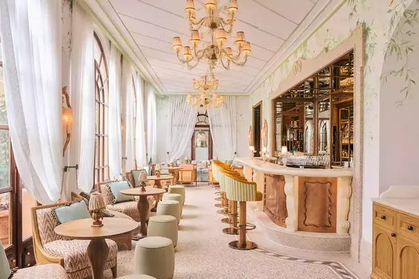 Elegant interior of a restaurant with a bar, ornate chandeliers, and seating areas by large windows
