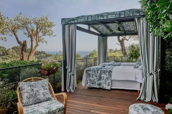 Outdoor cabana with a bed and lounge chairs on a wooden deck overlooking a scenic view