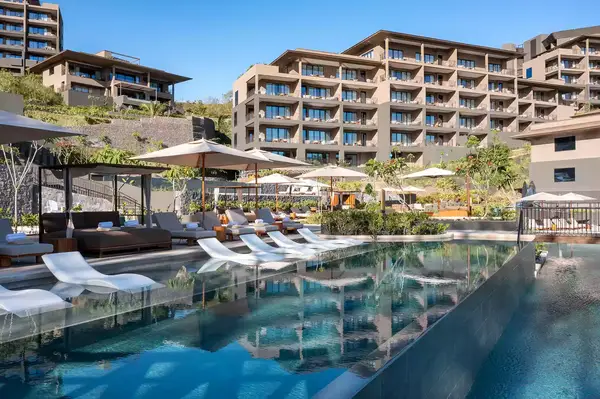 The pool area of a luxury resort with lounge chairs, sun umbrellas, and modern buildings in the background
