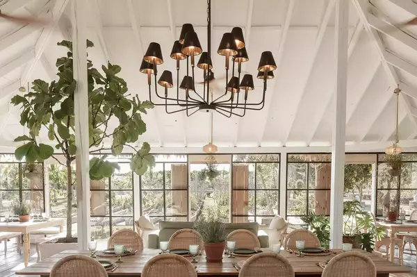 Dining area with chandelier, large wooden table, and surrounding greenery under a tent-like structure