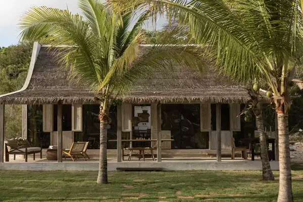 A small building with a thatched roof surrounded by palm trees and grass