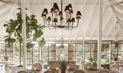 Dining area with chandelier, large wooden table, and surrounding greenery under a tent-like structure