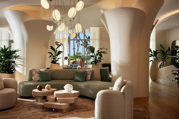 Modern hotel lobby area with stylish furniture and a decorative ceiling centerpiece, surrounded by plants and large windows with natural light