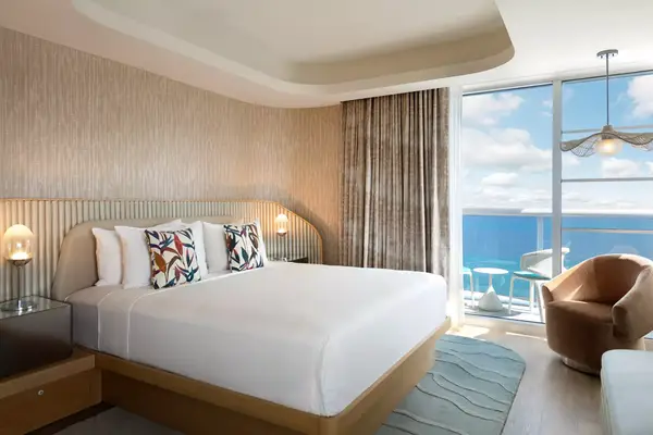Modern bedroom with a large bed, ocean view balcony in the background