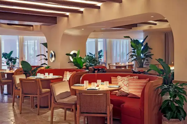 Interior of a restaurant with seating areas, tables, chairs, and potted plants as decor