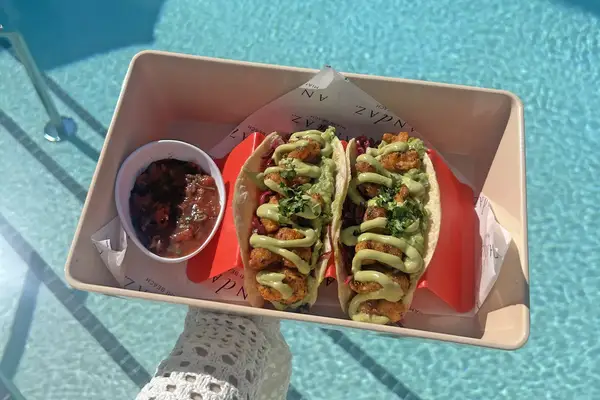 Tray with tacos and a side of salsa by a pool