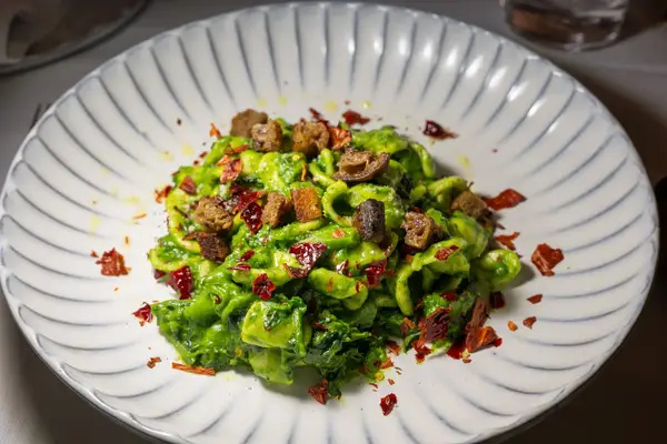 A plate of pasta with green sauce, croutons, and red chili flakes