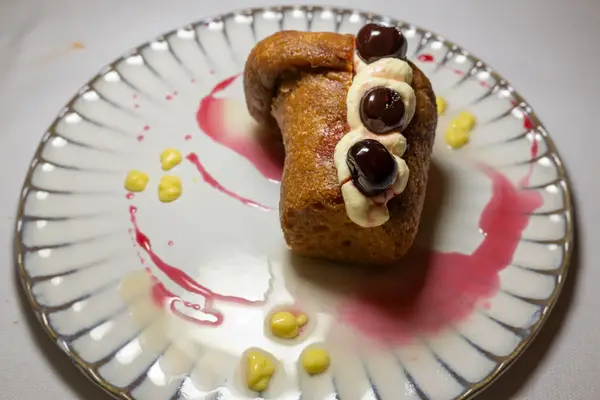 A plated dessert with a baked item garnished with cherries, cream, and sauce