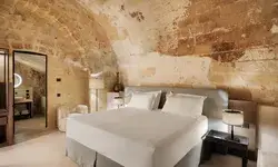 A cozy bedroom with a vaulted ceiling and rustic stone walls, featuring a double bed and minimalistic furnishings