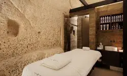 A luxurious spa treatment room with a stone wall backdrop, a massage table, and shelves filled with spa products