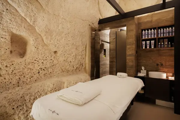 A luxurious spa treatment room with a stone wall backdrop, a massage table, and shelves filled with spa products
