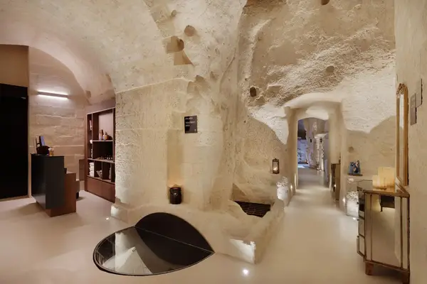 Underground chamber with carved stone walls, minimalist furniture, and wall cutouts showing shelves and decor elements