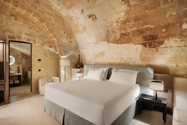 A cozy bedroom with a vaulted ceiling and rustic stone walls, featuring a double bed and minimalistic furnishings