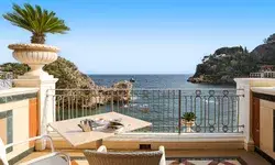Outdoor balcony with seating and table overlooking the sea, ornate railings, and distant coastal cliffs