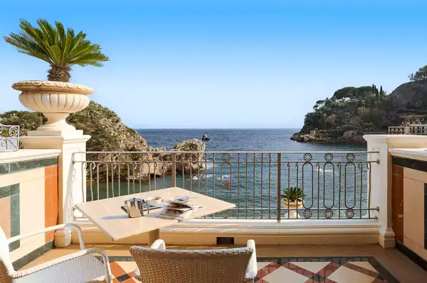 Outdoor balcony with seating and table overlooking the sea, ornate railings, and distant coastal cliffs