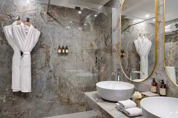 Elegant bathroom interior with a marble design, featuring a glass shower, round mirror, sink, and hanging bathrobes
