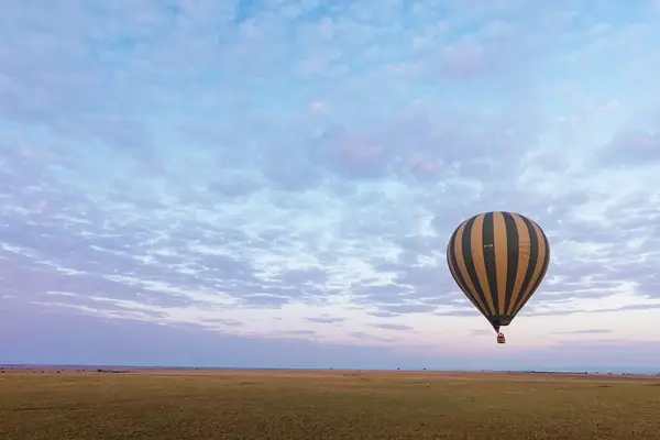 A hot air balloon floating above a grassy plain under a clouded sky
