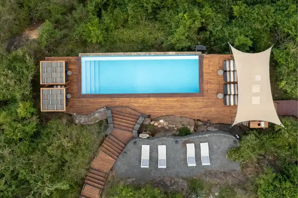 Aerial view of a pool area surrounded by greenery with loungers and a shaded seating area