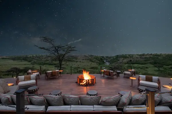 Outdoor deck with seating around a fire pit surrounded by grassy landscape under a starry night sky
