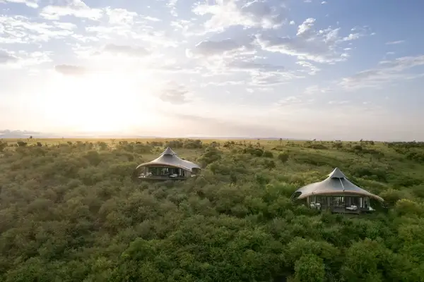 Two tentlike structures positioned amidst green vegetation with a scenic horizon and sky in the distance likely part of a lodge