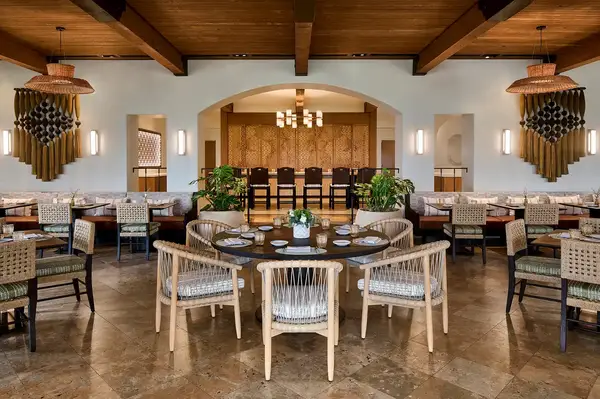 Restaurant interior with arranged dining tables and chairs, warm lighting, and a decorative backdrop