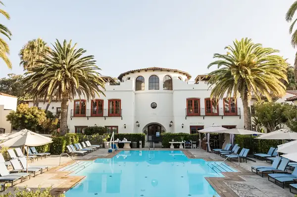 Outdoor pool area with lounge chairs and a Mediterranean-style building surrounded by palm trees at a resort