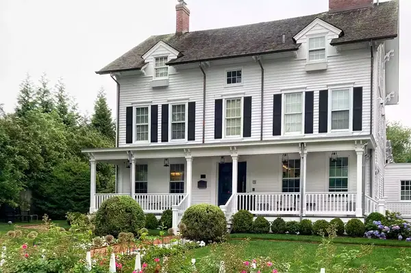 A traditional two-story house with a porch, surrounded by a garden