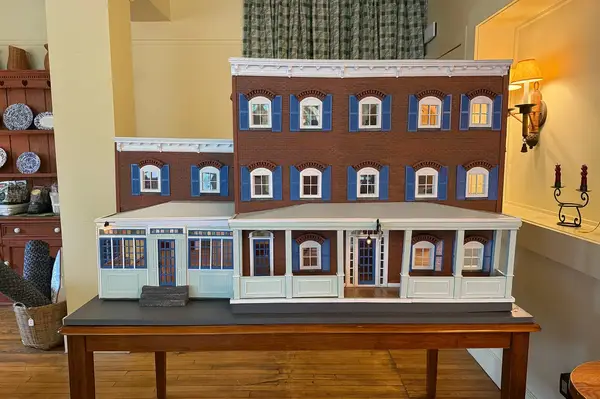 A detailed dollhouse model of a traditional-style building sitting on a wooden table indoors, showing architectural features