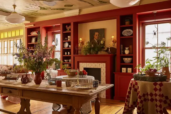 Interior of a rustic hotel room with flowers on a table and red walls featuring shelves containing various decorative items