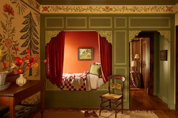 A hotel room with a decorative alcove containing a bed, surrounded by ornate wood paneling and floral wallpaper