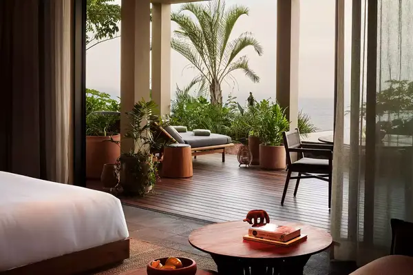 Luxury hotel room with a patio featuring plants, lounge chairs, and an ocean view