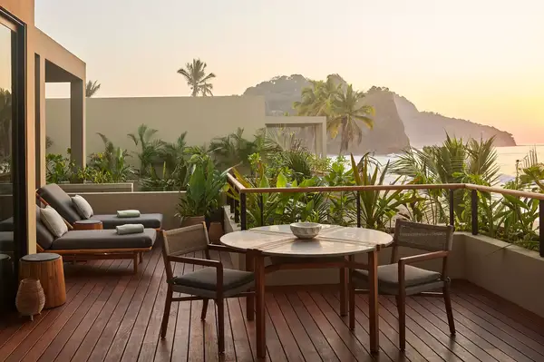 Beachfront suite terrace with outdoor seating, surrounded by lush foliage and ocean view during sunset