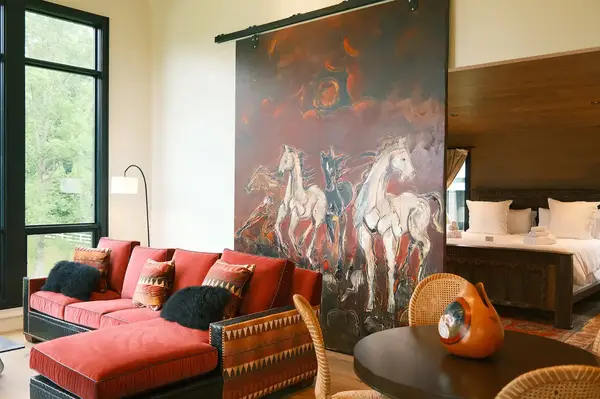 Interior of a cozy cottage with a red sofa, a large painting of running horses, and a bed in the background