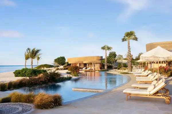 Luxury resort poolside with lounge chairs, palm trees, and a view of the beach in a landscaped setting