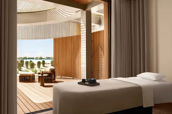 A spa room featuring a massage table and an outdoor patio with views of palm trees and water