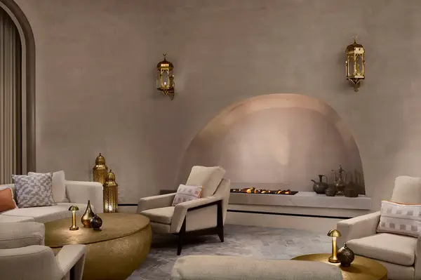 A softly lit, luxurious lounge area with armchairs, tables, and a curved fireplace set within an elegant architectural environment