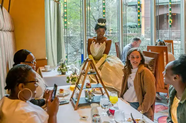 People dining at a table with a Disney princess character dressed as Tiana interacting with them