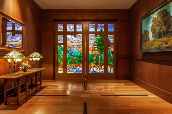 Room interior with stained glass doors depicting a park landscape and wooden furnishings including tables with lamps
