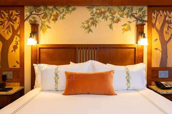 A guest room bed with a decorative orange pillow and nature-themed wall art