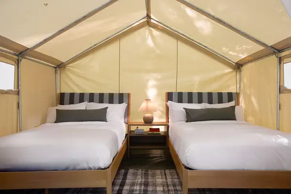 Interior view of a luxury tent featuring two neatly made beds with a shared nightstand and a central lamp