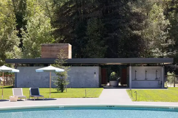 Outdoor pool facility with modern architecture in a forested setting, with a grassy area and lounge chairs in the foreground